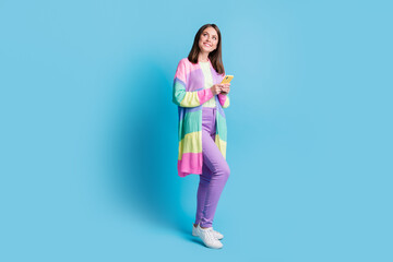 Fototapeta na wymiar Full length photo of pretty brown haired woman wear violet pants hold smartphone look empty space isolated on blue color background