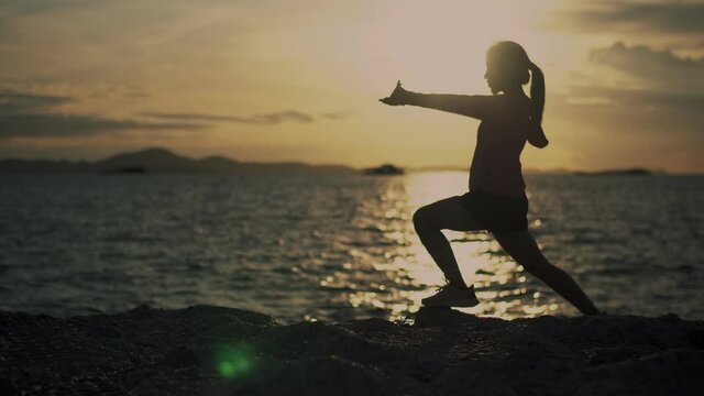 Silhouette of Asian woman working out runner stretching exercise on the beach at sunset. Athlete female in sportswear jogging outdoors during a beautiful sunset.