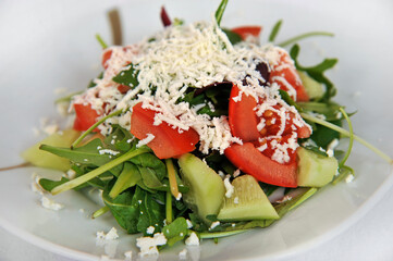 Fresh vegetable salad with tomatoes, cucumbers and arugula on a plate isolated on a white background. Selective focus.
