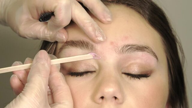 Brow master applying wax on the eyebrow of female face of a brunette woman. Wax correction of the shape of the eyebrows. Beauty industry. 