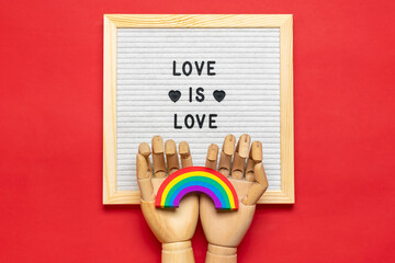 Felt board with quote, wooden hands holds rainbow with colors of LGBT isolated on red background...