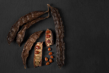 Seeds and pods of carob tree in close-up on black background - obrazy, fototapety, plakaty