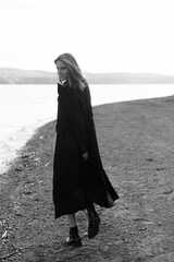 Young beautiful girl walking.  Summer landscape,good weather. Beach, sea. Windy day with sun and clouds. Cotton black dress eco style. Nature and freedom. Follow me. Long hair, big eyes and lips