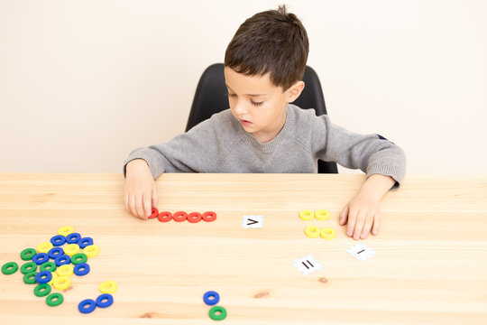 Preschool child plays a math game, interested, focused. Topic of comparing numbers, concepts of more than, less than, equal to that, smart boy. Little genius of mathematics. Caucasian. Copy space.