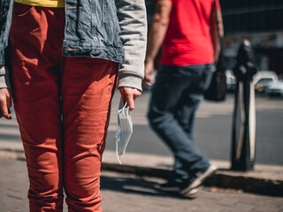 Girl having a medical protective mask off while standing in a populated area in the city. Person walking close to an unprotected teenager during pandemic