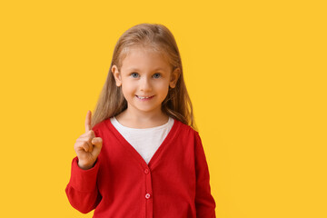 Cute little girl with raised index finger on color background