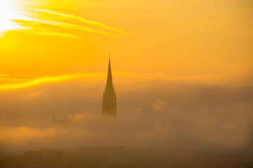 Fototapeta premium Church of the Sacred Heart of Jesus surrounded by fog and clouds, in Graz, Styria region, Austria, at sunrise. Beautiful foggy morning over the city of Graz, in autumn