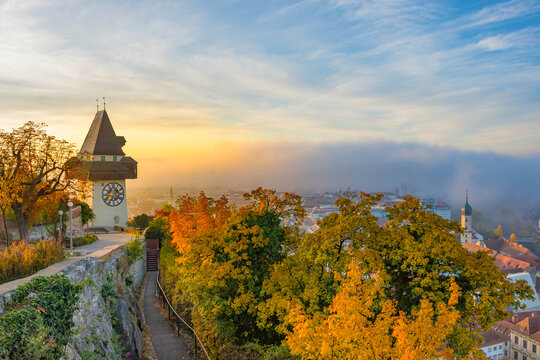 The famous clock tower on Schlossberg hill, in Graz, Styria region, Austria, at sunrise. Beautiful foggy morning over the city of Graz, in autumn