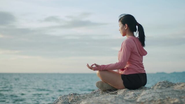 Asian athletic female meditating sitting while sunset. Zen yoga meditation practice in nature.