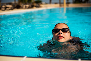 Fashion portrait of graceful cute girl in stylish sunglasses posing in the pool during holidays on luxury resort. Cheerful plus size teenage girl enjoying. happy, positive emotion, summer style.