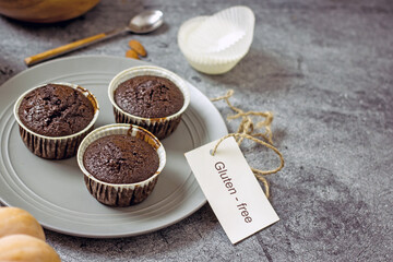 Gluten-free pumpkin chocolate muffins on a gray plate surrounded by ingredients, next to a white card for the inscription. Copy space, flat lei. Healthy baking concept