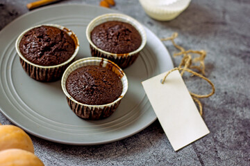 Gluten-free pumpkin chocolate muffins on a gray plate surrounded by ingredients, next to a white card for the inscription. Copy space, flat lei. Healthy baking concept