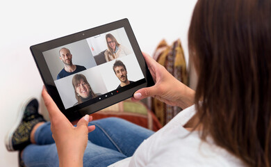 Fototapeta na wymiar Woman in video conference with a group of people. Girl at home with a tablet in her hands. Young woman resting in a sofa. Millennial girl. Online communications.
