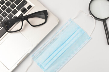 White office desk table face mask, magnifying glass. eye glass with laptop on white background. Work from home and covid-19 concept new normal. Selective focus.