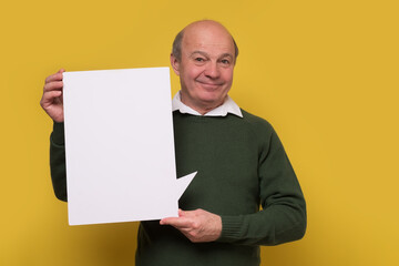 Senior man holding a blank placard on yellow wall.