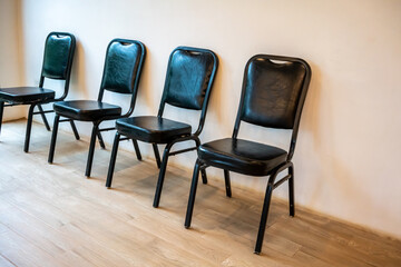 Row of black metal leather chairs on wooden floor against white wall - obrazy, fototapety, plakaty