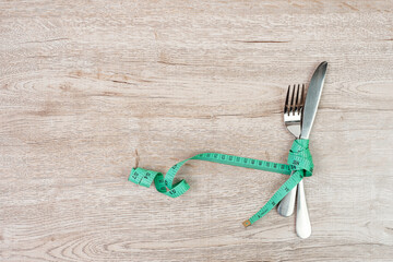 Top view Green Measuring tape wrapped around fork and knife on wooden table background. dieting, weight loss, obesity and food control concept