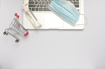 Shopping trolley and medical face mask with laptop on white background. Covid-19 pandemic. Online shopping. Selective focus.