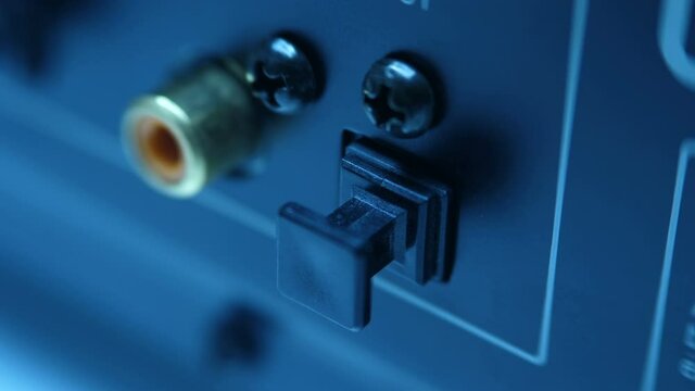 The optical output on the rear panel of the black stereo equipment is glows red. A hand removes the protective cap and inserts the plug of the optical cable into the connector of the audio deck