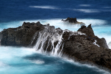 Detail of rocks with waterfalls of ocean water.