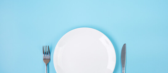 empty white ceramics plate with knife and fork on blue background. dining and kitchenware concept
