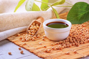 Soy sauce with soya beans scattered on a bamboo napkin against the background of burlap and branch young green pods soybean, closeup with selective focus
