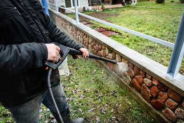 Cleaning dirty stone fence using high pressure power washer.