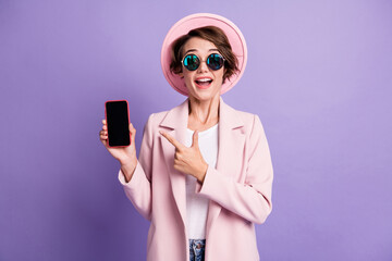 Photo of beautiful attractive surprised curly student girl dressed pink blazer headwear eyewear pointing phone isolated purple color background