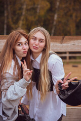 Two teenage girls with long hair, blonde and red, with a protective helmet in their hands fool around looking at the camera.