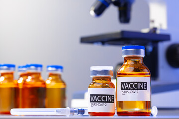 Vial of Covid-19 vaccine next to a microscope