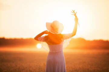 girl in a hat in a field of wheat at sunset in the sun