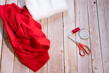 Step by step instructions. Step 1. Master class on creating a red hat of Santa Claus. Blanks, fleece fabric, scissors, and a red spool of thread lie on a wooden table.