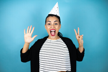 Young beautiful woman wearing a birthday hat over insolated blue background showing and pointing up...