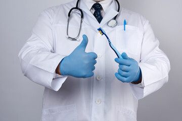 doctor therapist is dressed in a white robe uniform and blue sterile gloves is standing and holding a toothbrush