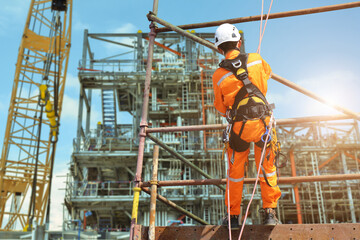 Safety concept, worker on high at scaffolding wearing equipment protective safety harness all PPE with rope for sprinkle from high area and structrue steel in construction site background.