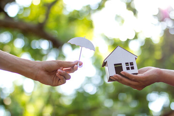 Hand giving an umbrella to protect a house metaphor insurance, loan or home financial concept.