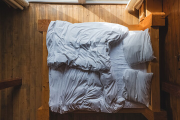 Bed with white bedding near the window in wooden house
