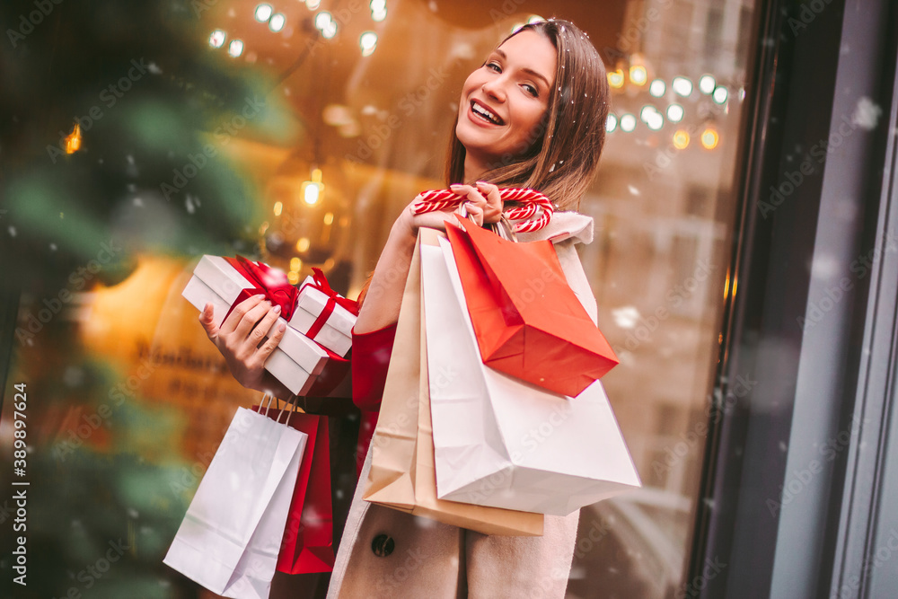 Wall mural beautiful happy girl hold shopping bags and gift boxes in hands and smile on city street. young attr