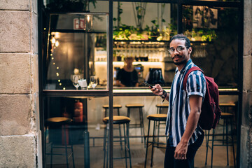 Fototapeta premium Positive ethnic man using smartphone in street cafe