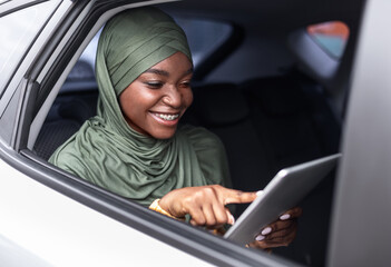 Cheerful Black Muslim Woman In Hijab Using Digital Tablet While Ridind Car