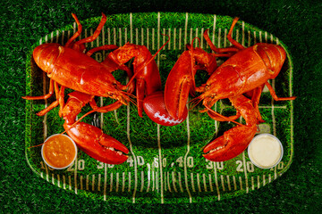 Two ready to eat lobsters with ball and dipping sauce on green plate.