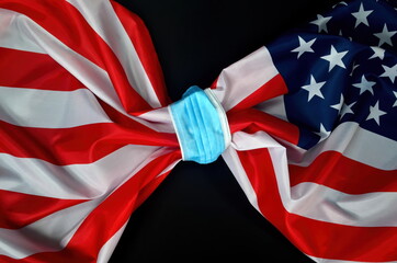 Flag of USA tied with a face protection mask. COVID - 19 problems in United States and in the world. Medicine, healthcare and virus concept. black background