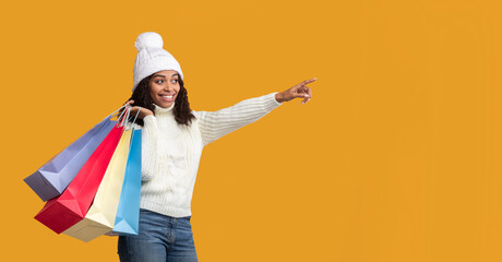 Black woman with shopping bags pointing at free space