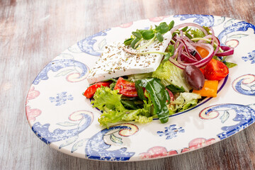 Greek salad on a decorative plate. On a wooden background