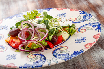Greek salad on a decorative plate. On a wooden background
