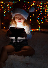 a little girl in a Santa hat sits near the Christmas lights with a lantern