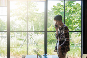 Young asian man talking on the smartphone and doing remote job using modern technologies checking installation of application on laptop and tablet while surfing net searching information. Vintage tone