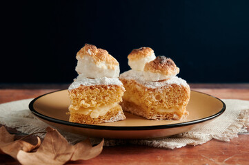 Sponge cake filled with cream and meringue on top. wooden table with black background.