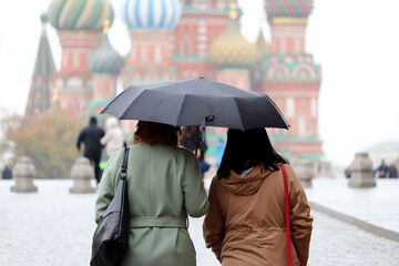 Rain in a Moscow, two women in autumn coats with one umbrella walking on the Red Square on...