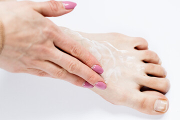 White cream on a woman's leg on a white background .Woman at home spa creaming her feet close up photo